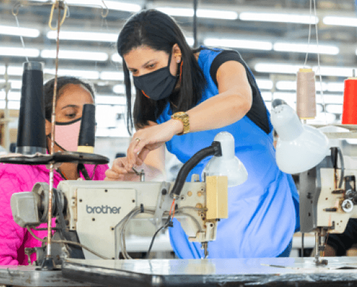 Foto de duas mulheres em uma fábrica, ajustando uma máquina de costura industrial